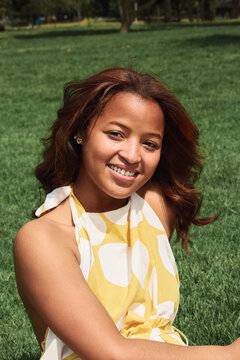 Young woman smiling outdoors sitting on grass enjoying summer