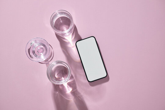 Smartphone and glasses of water on pink surface