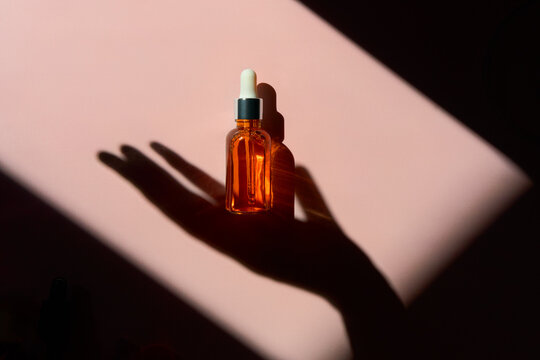 Glass Serum Bottle with Hand Shadow on Pink Background with Copy Space