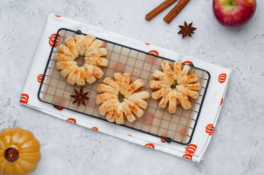 Apple rings in puff pastry on cooling rack, autumn baking flat lay with cinnamon and star anise