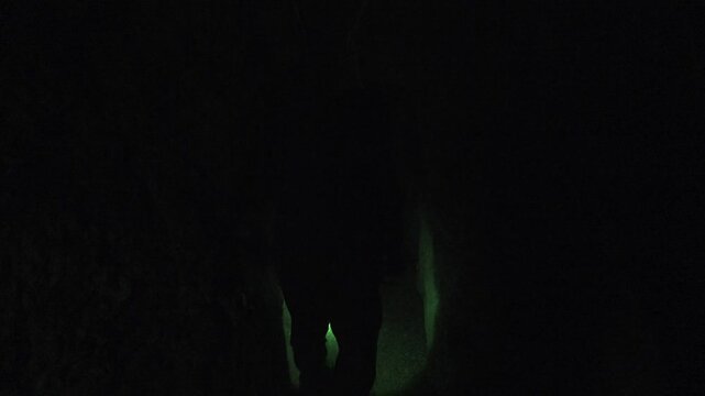 Researcher walks deep inside cave passage, lone explorer moving through dark underground chamber.