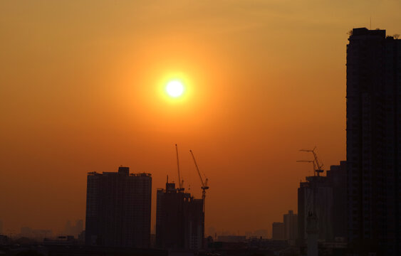 Bright sun shining on golden orange sky over groups of skyscrapers