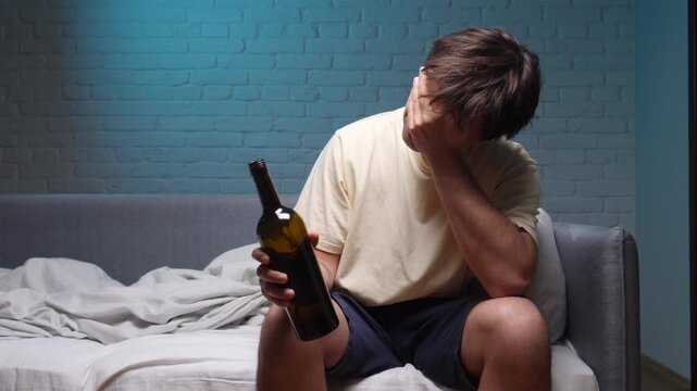 Man sits alone on a bed in a dim bedroom holding an empty wine bottle, drained and despondent, portraying alcoholism, depression and the silent struggle of addiction and hopelessness