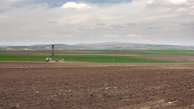 Artesian well drilling rig working on treeless farmland, opening water borehole on plain.