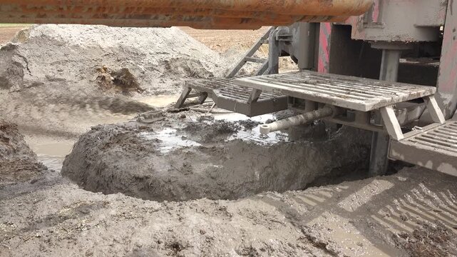 Drilling rig bores an artesian well while muddy water circulates around active equipment.