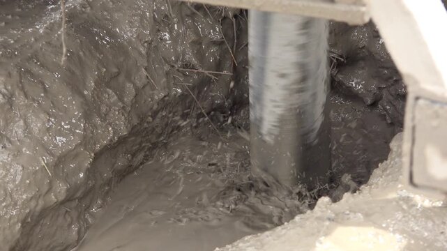Drilling rig bores an artesian well while muddy water circulates around active equipment.