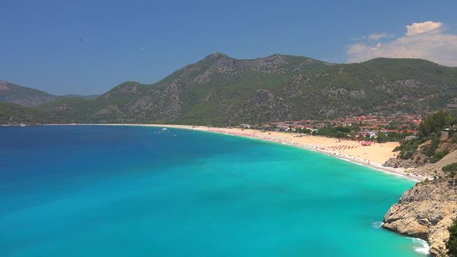 Fethiye Turkey beach shows turquoise sea, sandy bay, mountains, and paragliders above the coast.