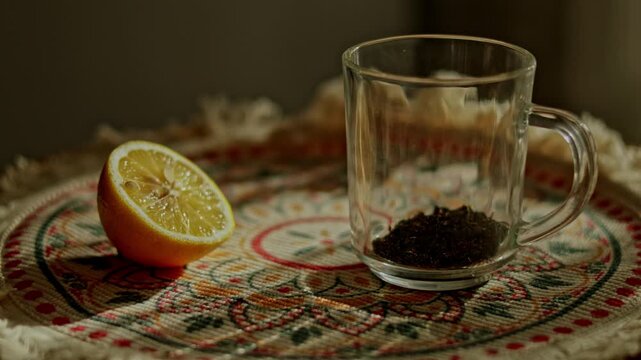 Pouring hot water over loose black tea in glass mug with lemon, brewing process close up