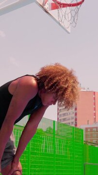 vertical Tired athlete resting on an urban basketball court