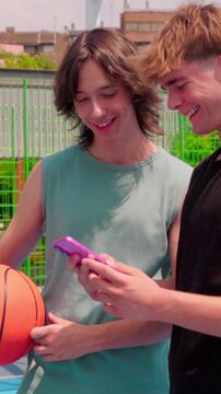 vertical Two young friends watching a phone on a basketball court