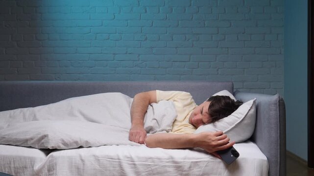 Young man sleeping soundly on his back in bed with a smartphone clutched in his hand, illustrating themes of technology addiction, screen time, and interrupted rest at night