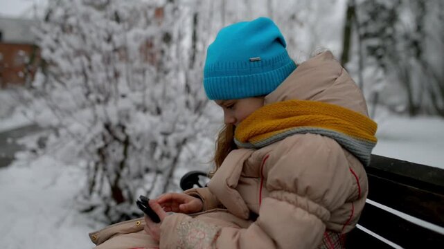 girl sits on bench in winter park with phone