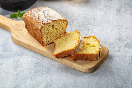 Sliced pound cake dusted with powdered sugar on wooden cutting board, soft yellow crumb texture visible, mint garnish beside, gray stone background