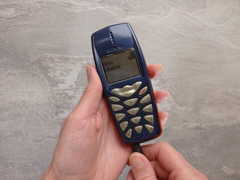 Close up of a person's hands charging an old Nokia 3510i mobile phone.