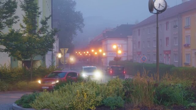 Olomouc, Olomouc Region, Czechia - 22 September 2026: View of a foggy street in Olomouc at dawn with glowing streetlights and a public clock.