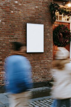 Christmas wreath and garland on a warm front door beside a blank mockup poster on a textured brick wall for holiday advertising
