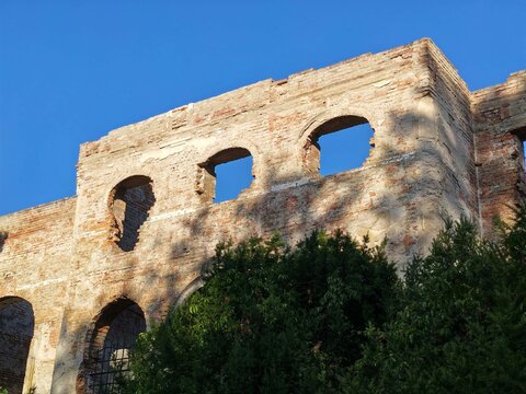 An old historic brick ruin with arched windows and green foliage against a clear blue sky.