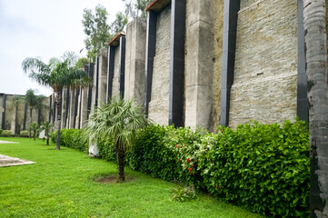 Architectural Contrast: A long, multi-textured outdoor wall featuring natural, rugged stone sections alternating with sleek, smooth concrete pillars, creating a striking modern landscape design. © Zeshan Aslam