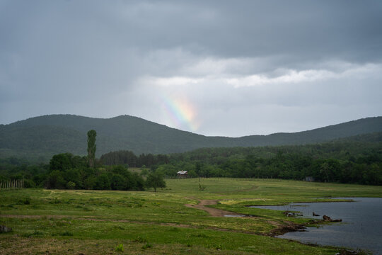 View of a rainbow over the green hills and lake near the Zhrebchevo Reservoir in Sliven, Bulgaria.