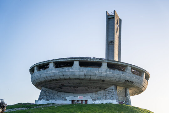 View of the abandoned Buzludzha Monument with its iconic saucer-shaped concrete structure and tall tower set against a clear blue sky in Stara Zagora, Bulgaria.