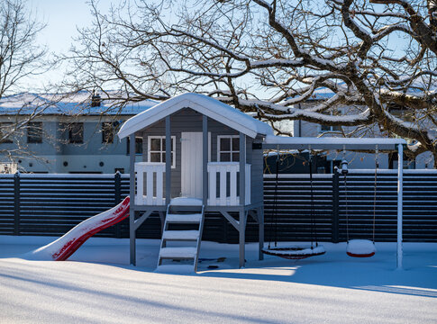 View of a wooden playhouse with a slide and swings covered in fresh snow in a backyard in Vilnius, Vilnius County, Lithuania.