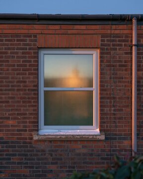 Single lit window in a dark brick wall during extreme cold, featuring a glowing misted pane and snow for fuel poverty and housing themes