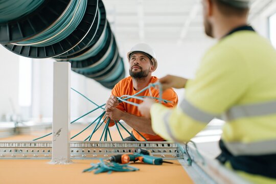 Floating cable drums hover over a man in a hard hat working in a dusty, unfinished server room for infrastructure and data center marketing