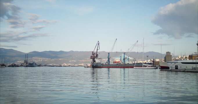 Rijeka, Primorje-Gorski Kotar, Croatia - 19 September 2026: View of the industrial harbor with cargo ships and cranes docked against a backdrop of mountains.