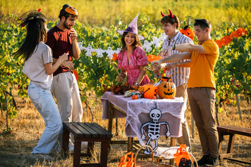 Obraz premium Group of cheerful friends celebrating Halloween with party props outdoors in a vineyard.