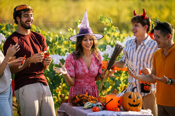 Obraz premium Close-up of smiling friends in Halloween costumes showing props at a vineyard party.