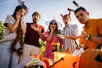 Obraz premium Group of surprised friends in Halloween costumes making shocked expressions towards the camera at an outdoor party.