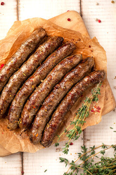 Juicy roasted grilled sausages served on parchment paper on wooden cutting board with herbs and spices