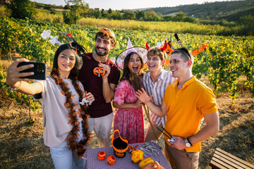 Obraz premium Young woman taking a group selfie with friends in Halloween costumes in a sunny vineyard.