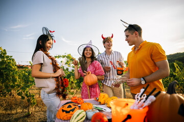 Obraz premium Friends in Halloween costumes chatting and laughing around a decorated party table outdoors.