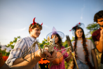Obraz premium Close-up of a hand holding a skeleton bat prop with blurred friends in Halloween costumes.
