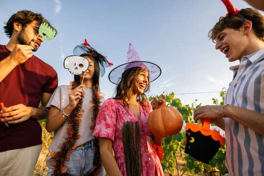 Young woman holding a pumpkin prop while laughing with friends at a Halloween party.