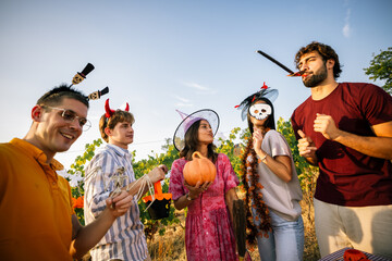 Obraz premium Group of energetic friends dancing and posing in Halloween costumes in a vineyard.