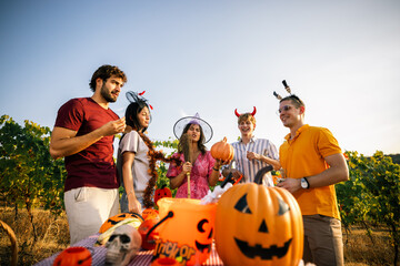 Obraz premium Group of friends celebrating Halloween outdoors around a decorated table in a vineyard.