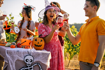 Obraz premium Happy woman in witch hat raising a glass of wine at a Halloween party with friends.