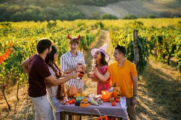 Obraz premium Wide shot of young friends in costumes having fun and toasting with red wine in a sunny vineyard landscape.