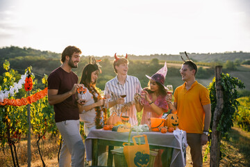 Obraz premium Group of friends talking and laughing around a Halloween-themed table set up in a sunny vineyard.