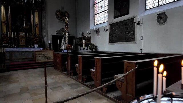 Augsburg, Bavaria, Germany - 12 October 2024: View of the interior of St. Markus Kapelle featuring lit votive candles on a stand in the foreground and wooden pews.