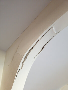 Structural cracking and flaking plaster on interior arch soffit caused by earthquakes and house settling