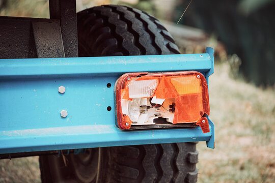 Close up of a damaged, broken tail light on the rear of a blue utility vehicle trailer with a tire visible