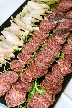 Salami slices and cured pork fat back lard with fresh arugula on a black slate platter. Gourmet cold cuts meat board, traditional Italian antipasto appetizer, catering food background.