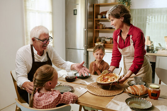 Middle aged Caucasian woman serving freshly baked pie to senior man and female children at table. Image useful for multigenerational family lifestyle and culinary advertising