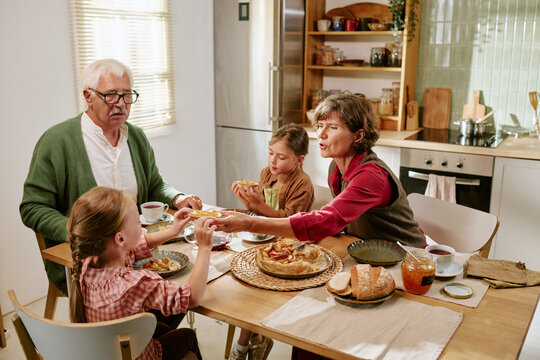 Senior Caucasian grandparents enjoying breakfast with grandchildren at home table, sharing pastry with jam. Concept suitable for family lifestyle, senior care or multigenerational ads