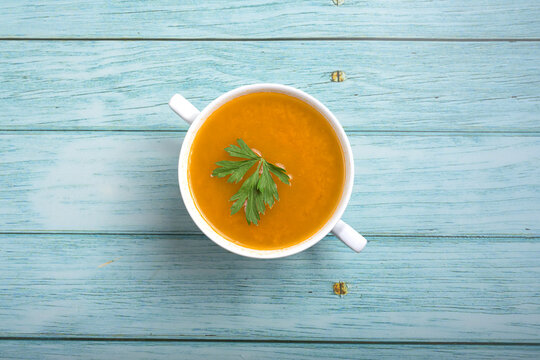 Hot homemade soup broth served in a white ceramic mug on a light blue wooden planks table background with copy space for food photographyKeywords