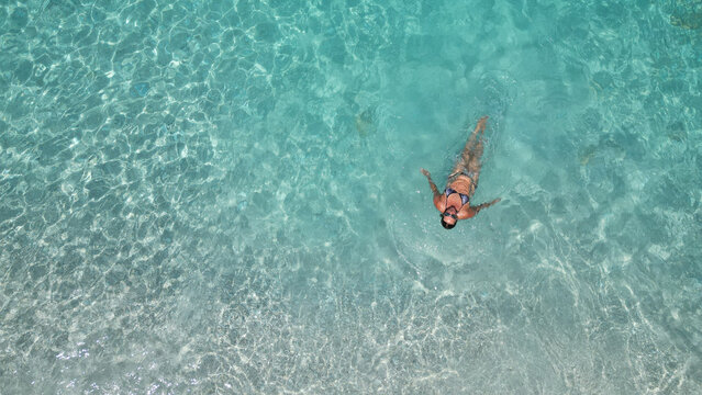 Aerial view of woman floating in clear turquoise sea water at Petani Beach in Kefalonia