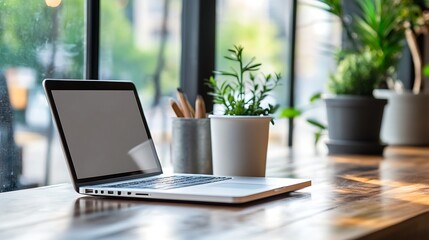 Fototapeta premium Modern workspace with open laptop potted plants and office supplies near a bright window